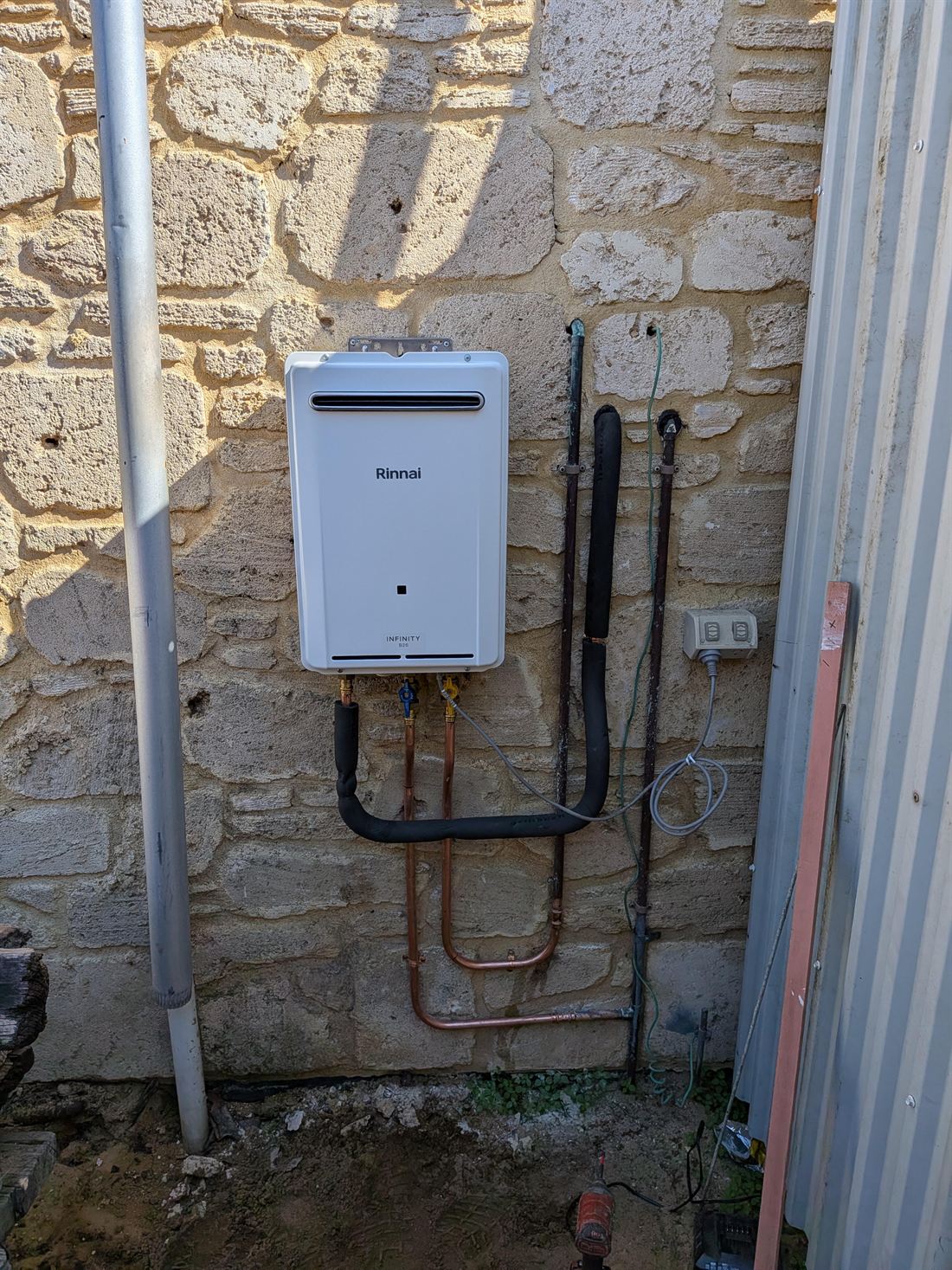 A continuous-flow gas hot water unit installed by HQ on a limestone wall, with new copper pipework